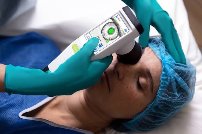 Medical professional using a handheld digital pupillometer to examine a patient's eye during a procedure.
