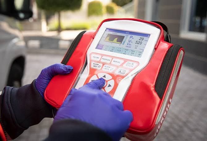 Gloved hands operating a portable medical ventilator monitor inside a red protective case.